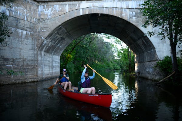 two women paddle a red canoe under the arch of a concrete bridge