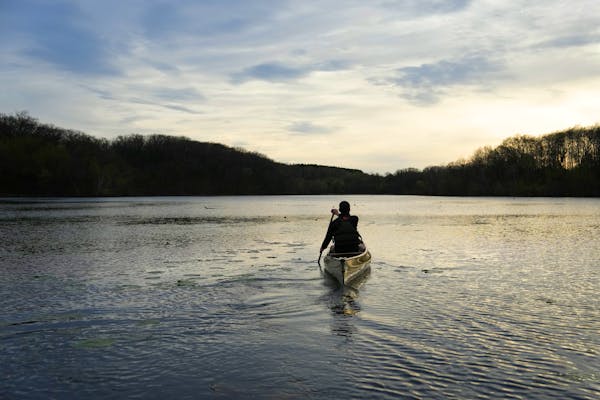a man paddles a solo canoe through a vast lake as the sun sets