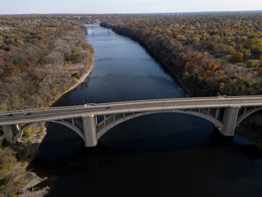 the span of a car bridge crosses a river gorge surrounded by trees showing fall leaf colors 